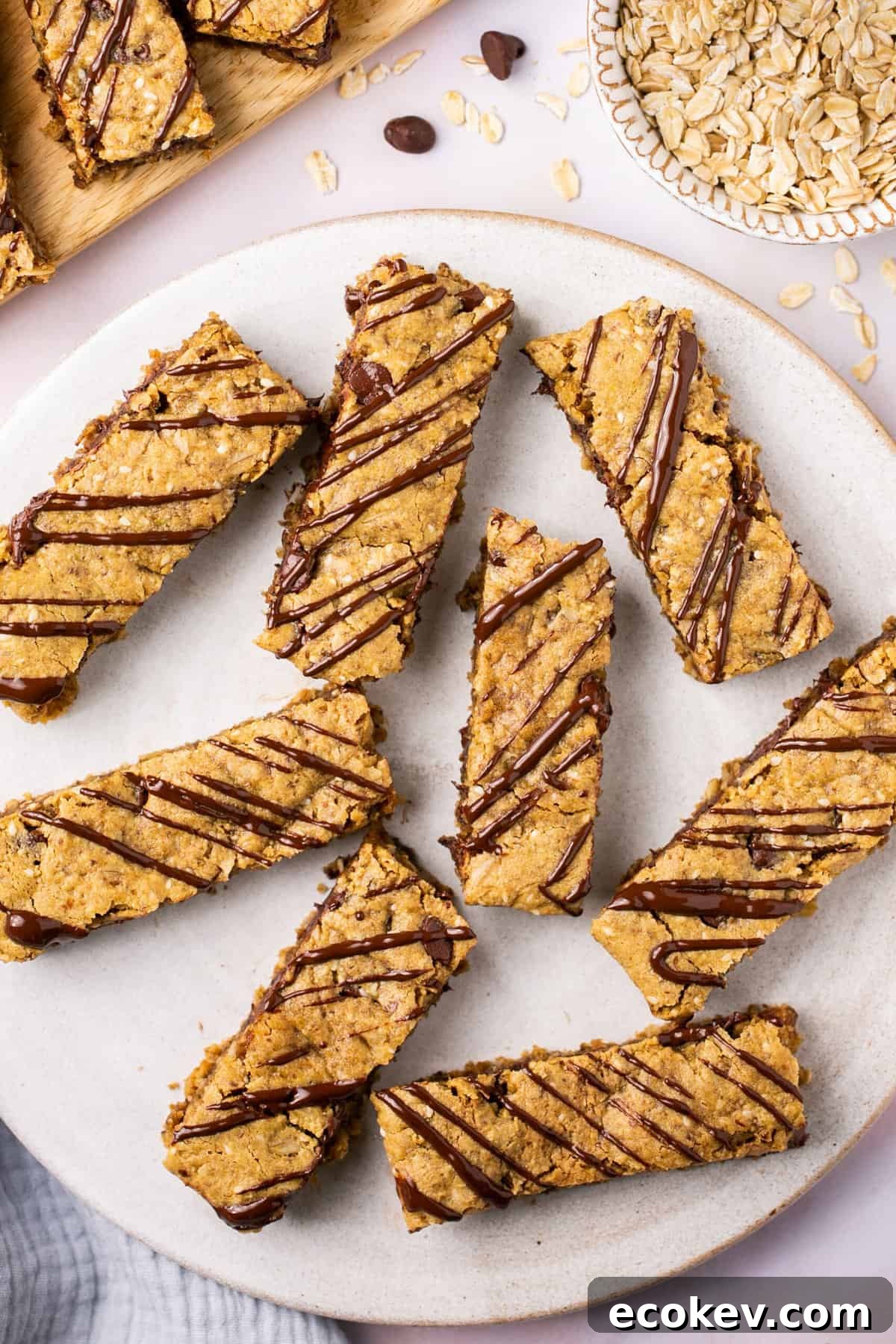 Lactation bars drizzled in chocolate on a plate with a bowl of oats beside it.