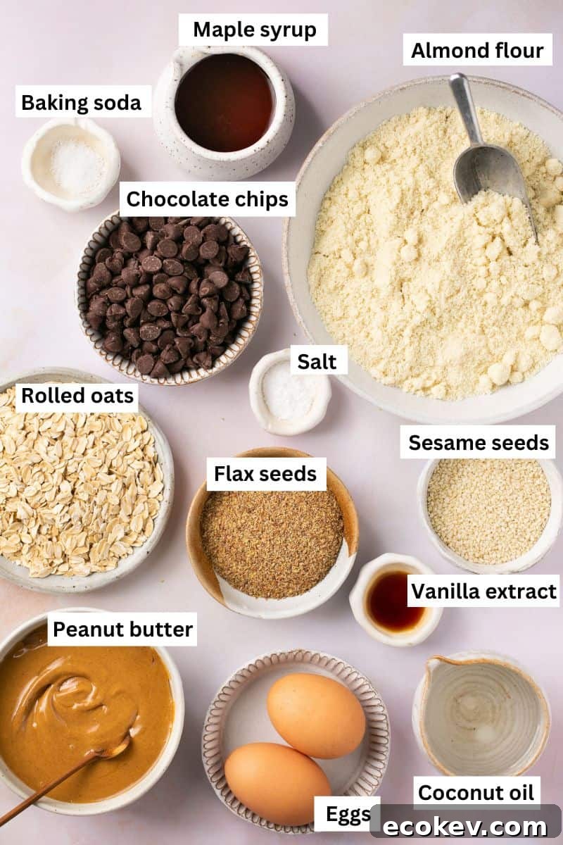 Baking ingredients separated into bowls including almond flour, oats, maple syrup, sesame seeds, flax seeds, chocolate chips, eggs and baking soda.