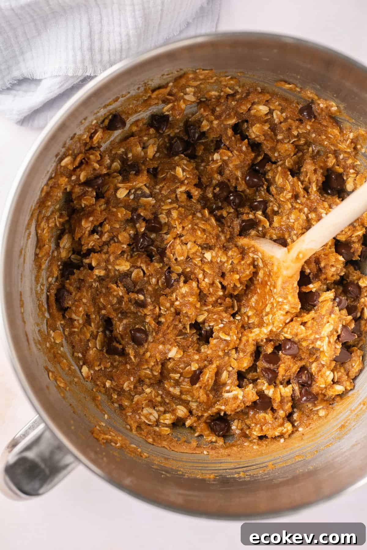 Chocolate chips being stirred into a sticky dough in a bowl.