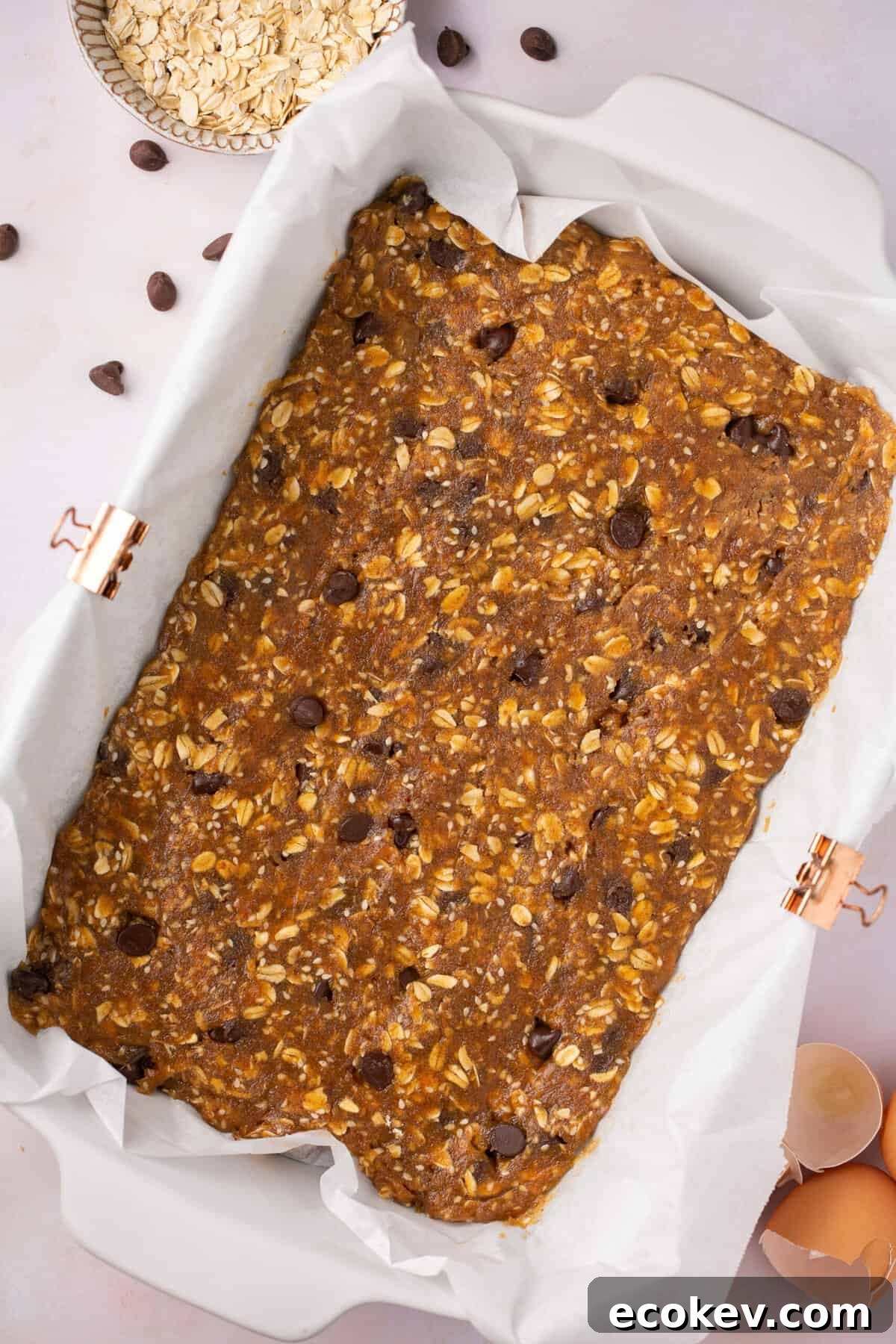 A 9 inch by 11 inch pan lined with parchment paper with chocolate chip granola batter in it.