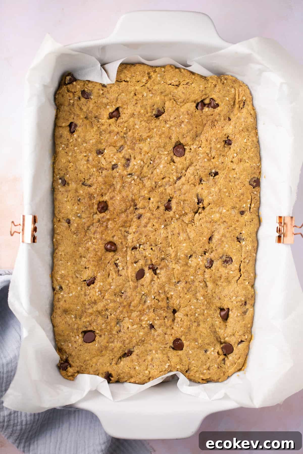 A pan lined with parchment paper with cooked chocolate chip granola bars in it.
