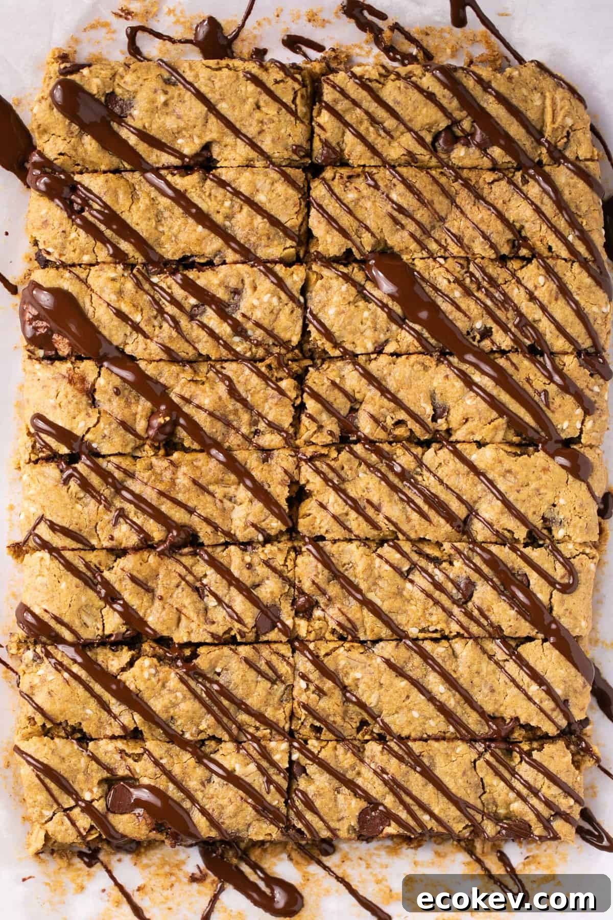 Chocolate chip granola bars that have been drizzled in melted chocolate on a piece of parchment paper.
