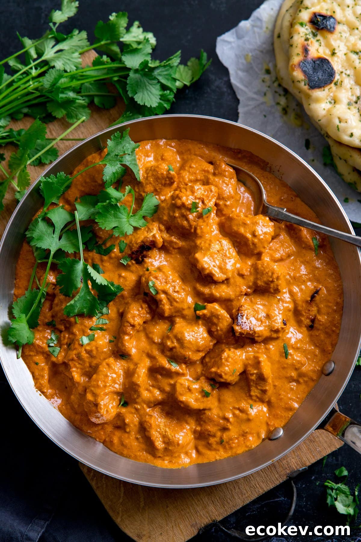 Overhead image of a pan filled with butter chicken curry, topped with fresh coriander. Naan bread just in shot.