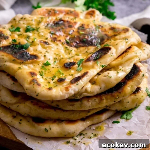 Pile of garlic naan breads on a piece of parchment on top of a wooden board.