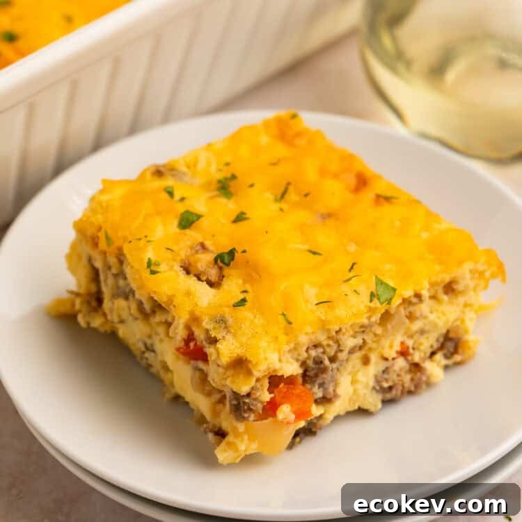 Slice of egg bake on a white plate with the casserole in the background in a white dish.