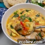 close up of spoon full of sausage, tortellini and veggies in creamy broth