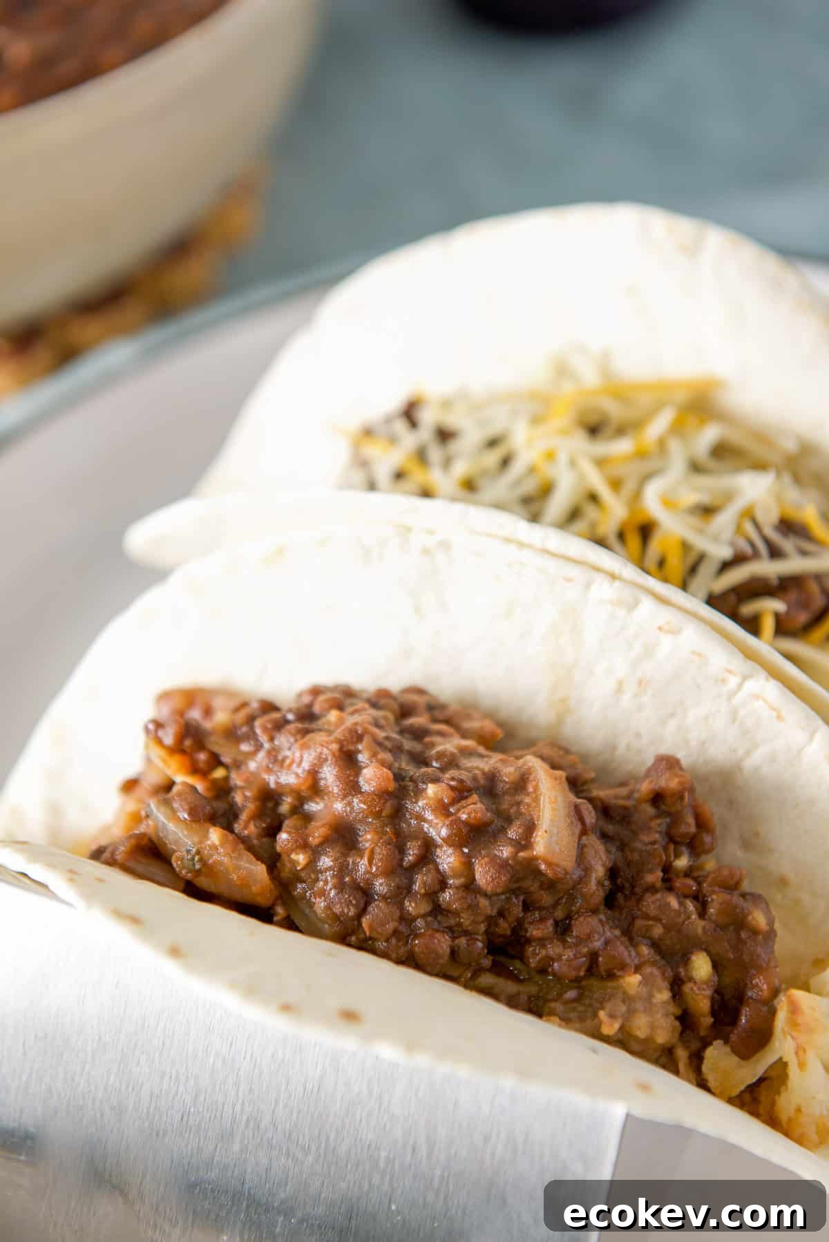 Close up of two flour tortillas in a taco holder with the lentils - one with cheese the other without