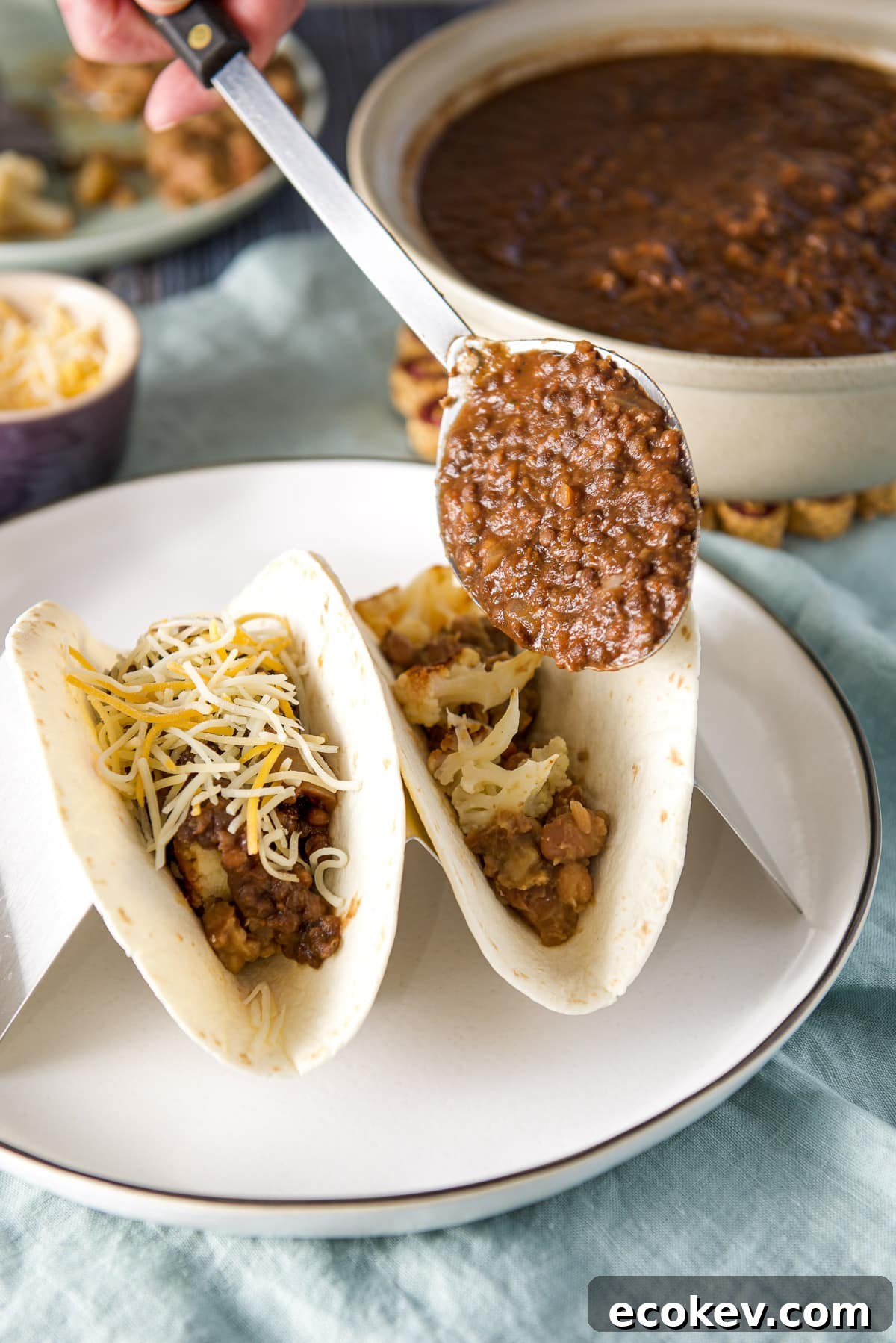 A large spoon of lentils held over the two flour tortillas with a big bowl in the background