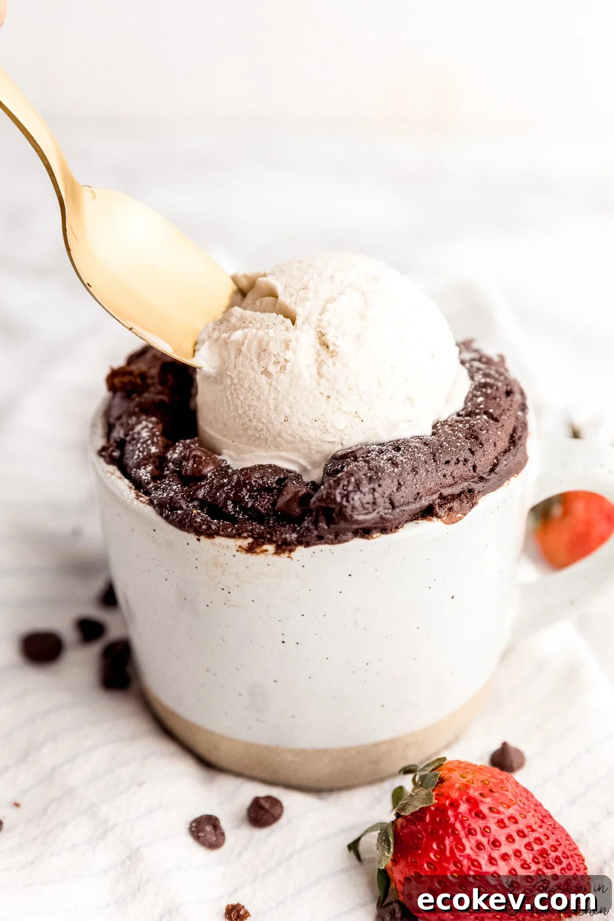 Close up photo of mug cake with a scoop of ice cream on top with spoon scooping some ice cream out.
