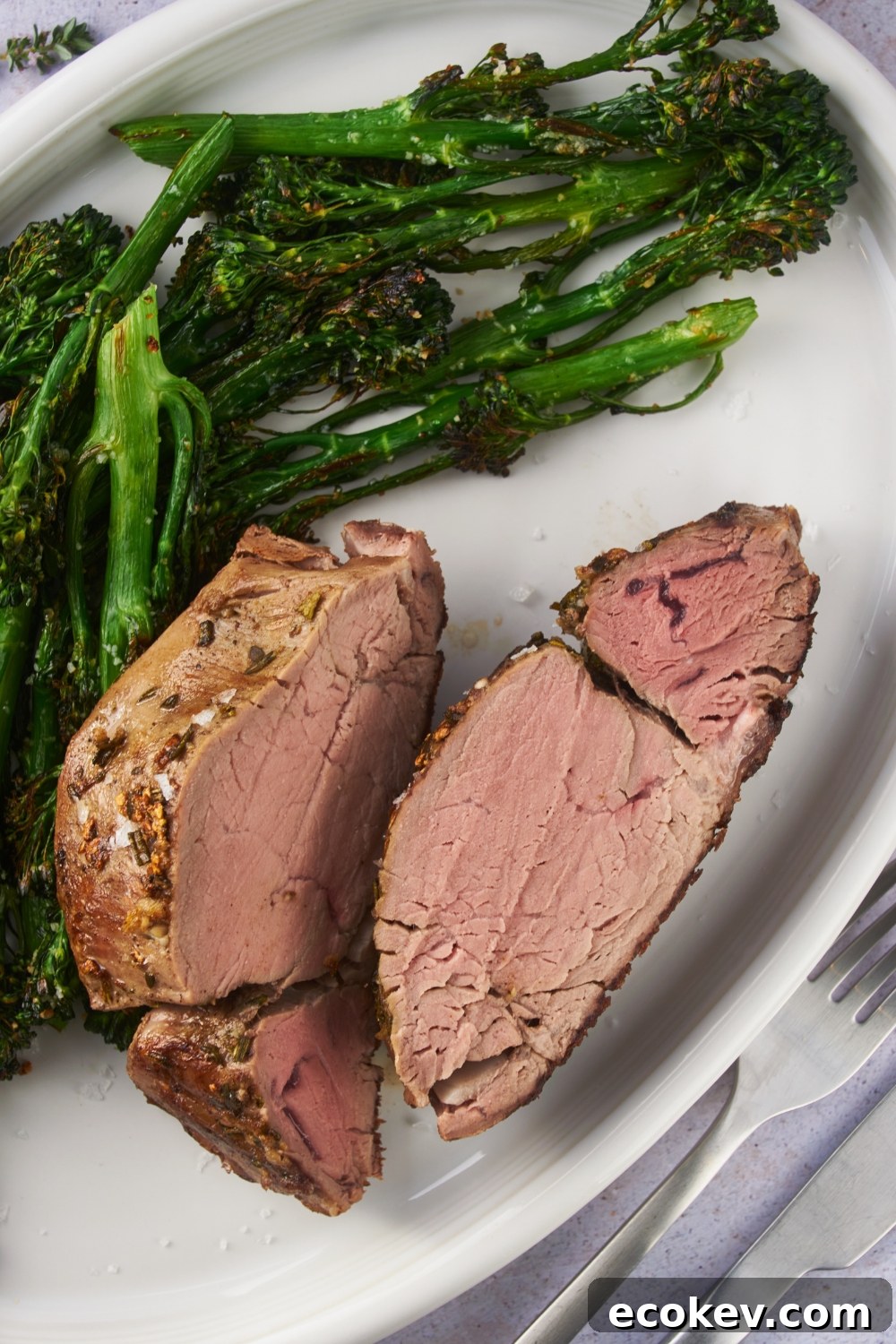 Beef tenderloin sliced in half on a white serving plate with a side of broccoli.