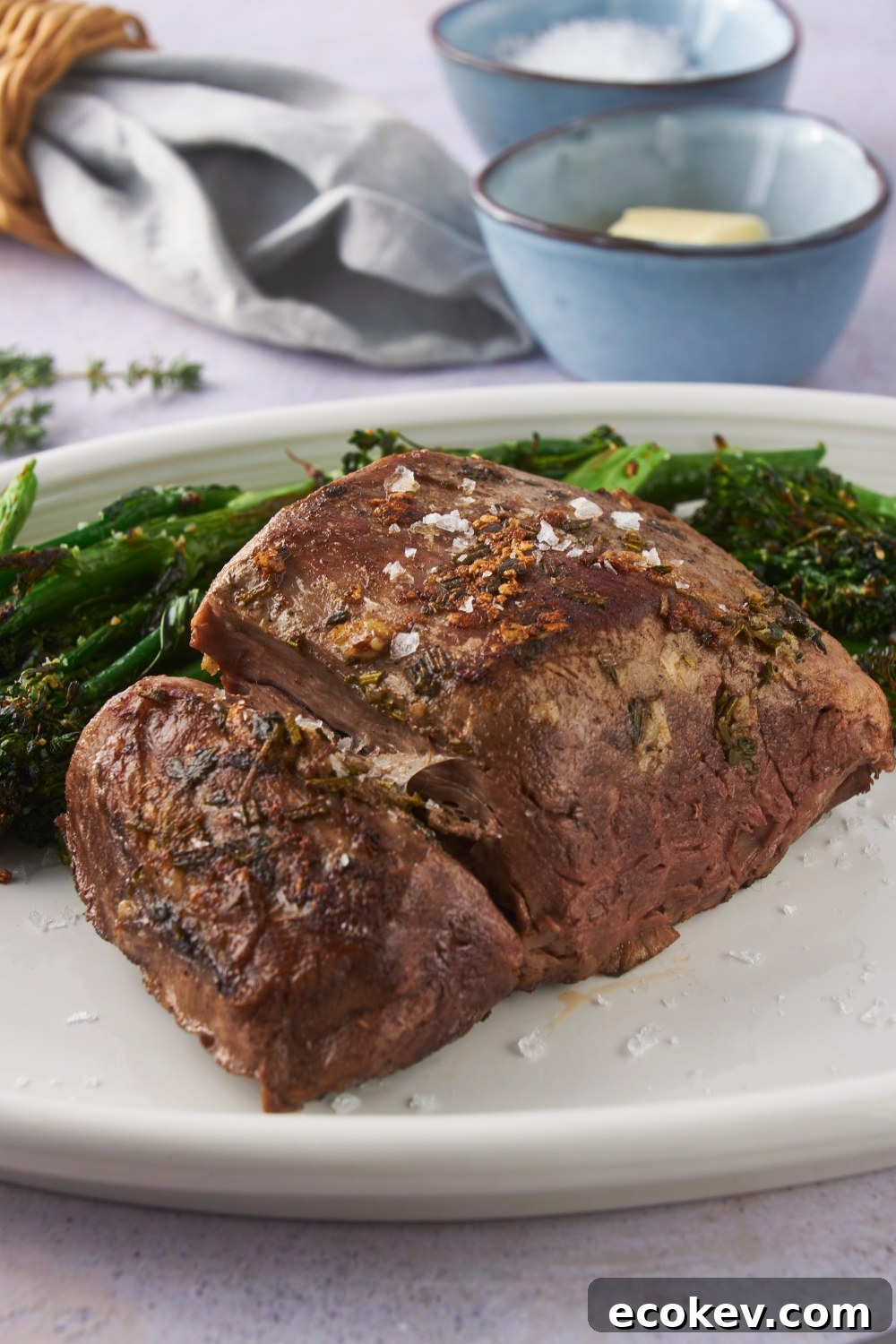 A seasoned beef tenderloin garnished with sea salt on a white serving plate with a side of broccoli.