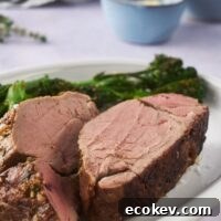 Close up of cooked beef tenderloin sliced in half on a white serving plate with a side of broccoli.