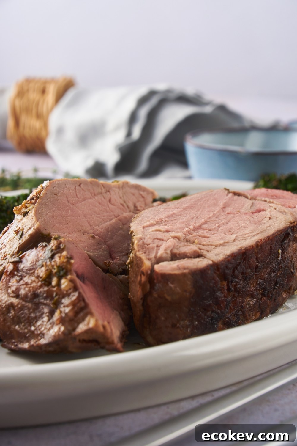 Close up of cooked beef tenderloin sliced in half on a white serving plate.