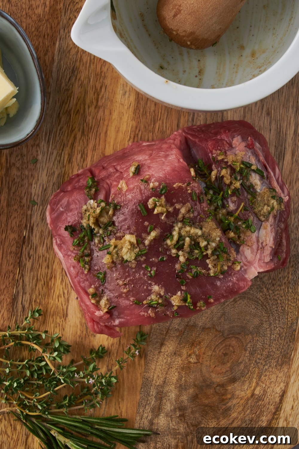 A beef tenderloin seasoned with herbs and garlic on a wooded board.