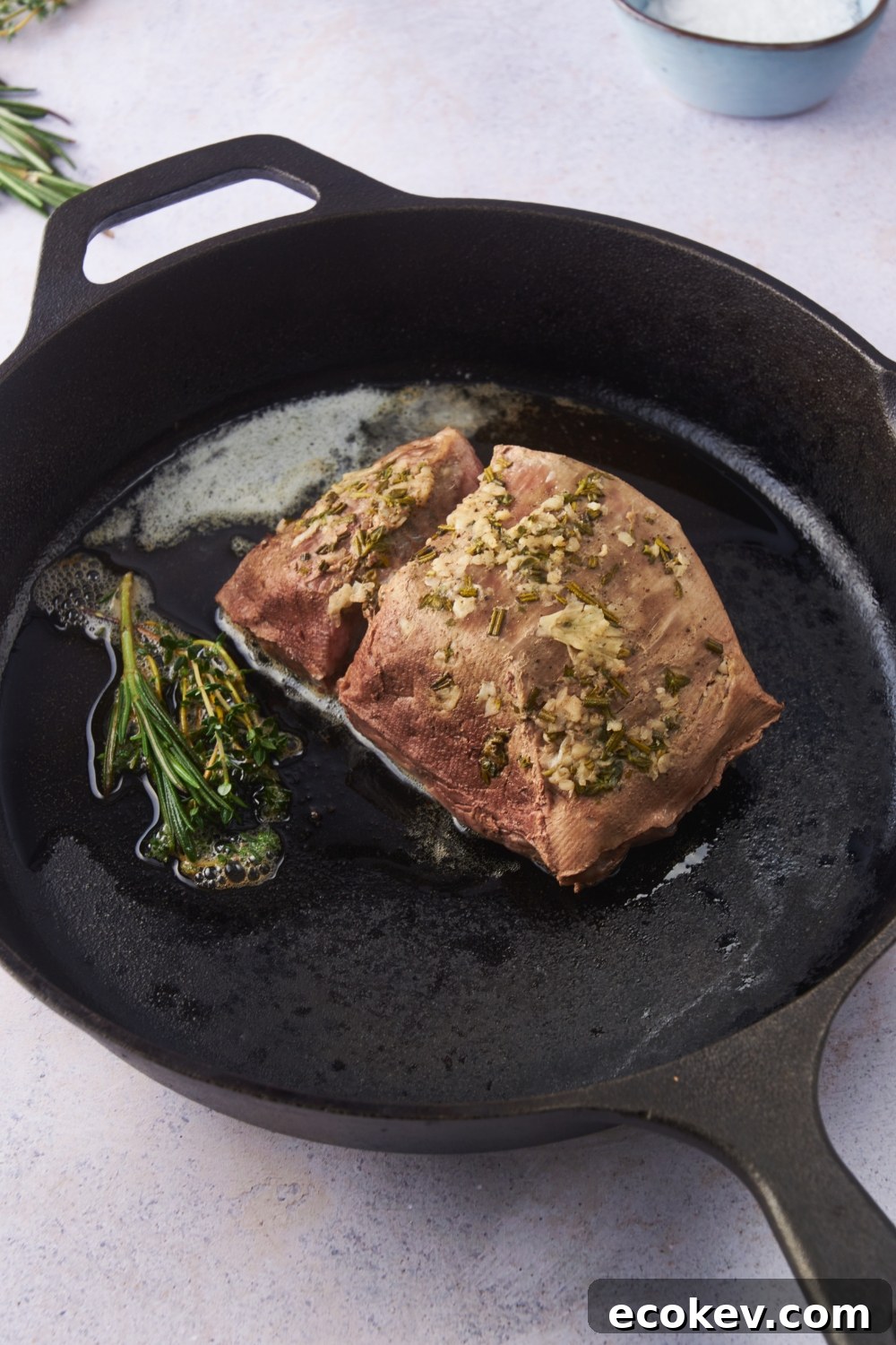 Cooked beef tenderloin in a cast iron skillet with fresh herbs.