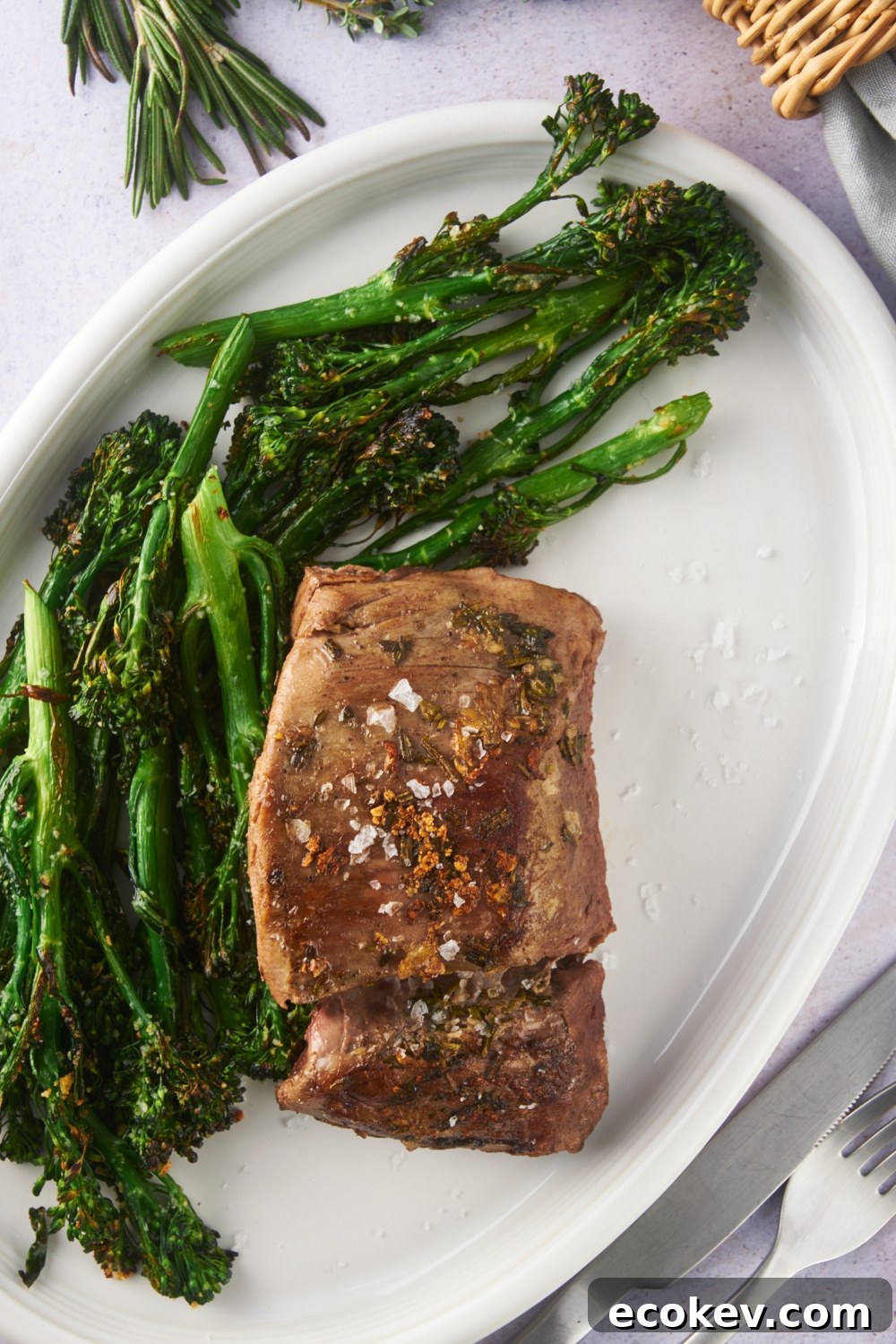Overhead view of seared beef tenderloin on a white serving plate with a side of broccoli.