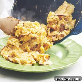 Wooden spatula pushing Matzoh Brei from a skillet to a plate.