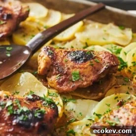 Spoon resting on a baking sheet of Roasted Marinated Chicken and Potatoes.