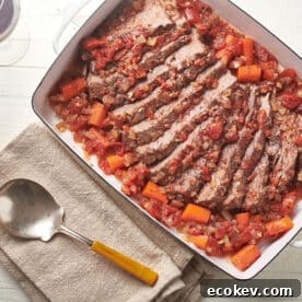 Jewish-style brisket in white dish on table with serving spoon.