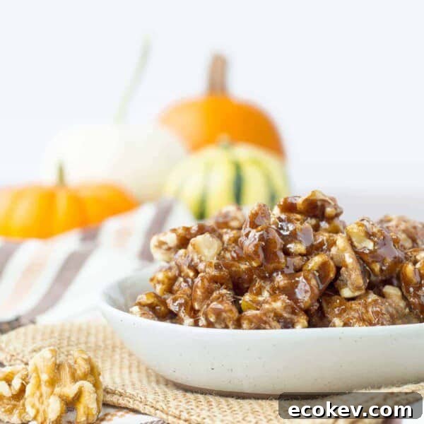 A bowl of pumpkin spice candied walnuts on a table with orange pumpkins in the background.