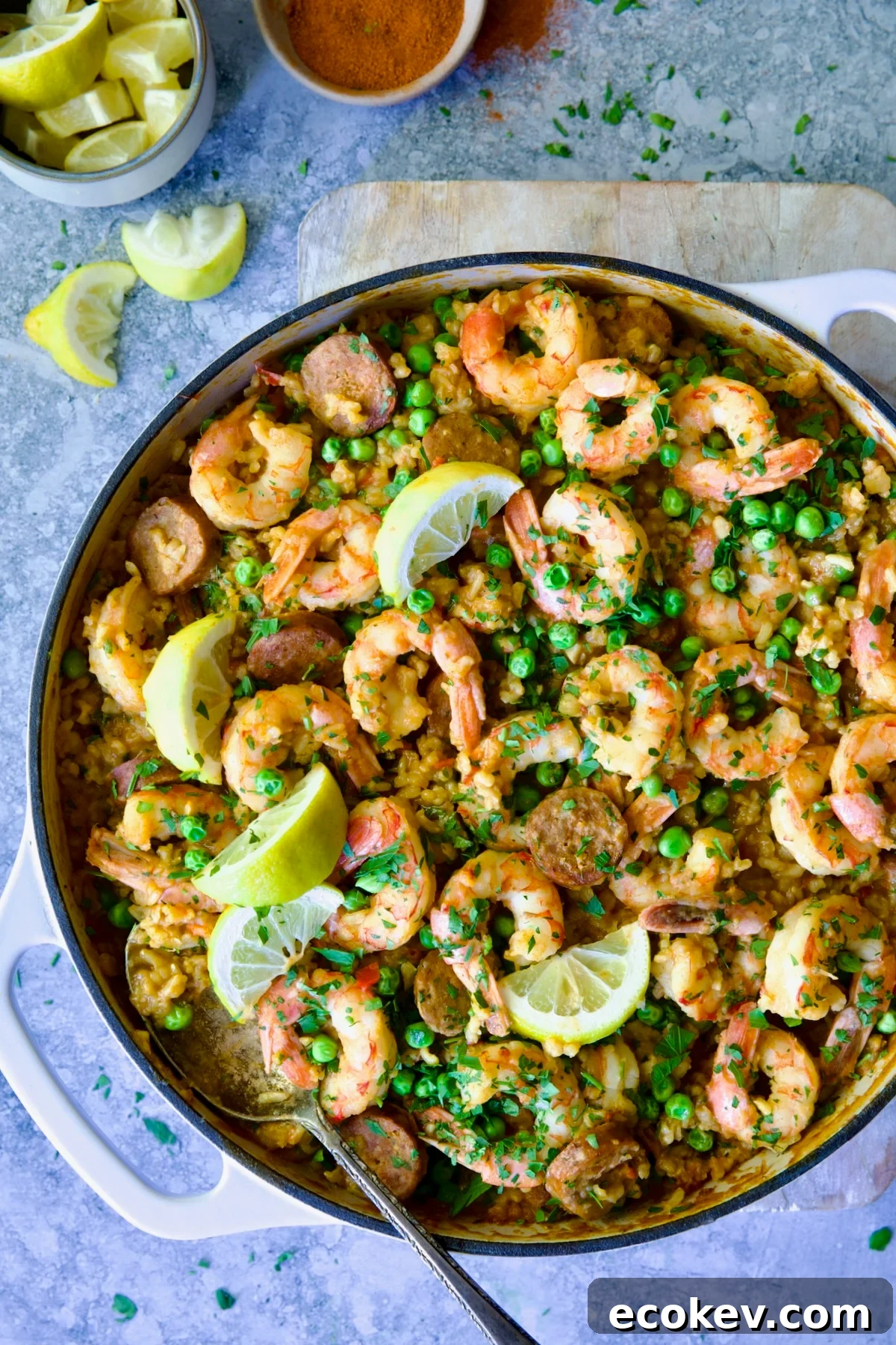 Brown Rice Paella with Shrimp and Chorizo in white enamel cast iron skillet on wood cutting board.