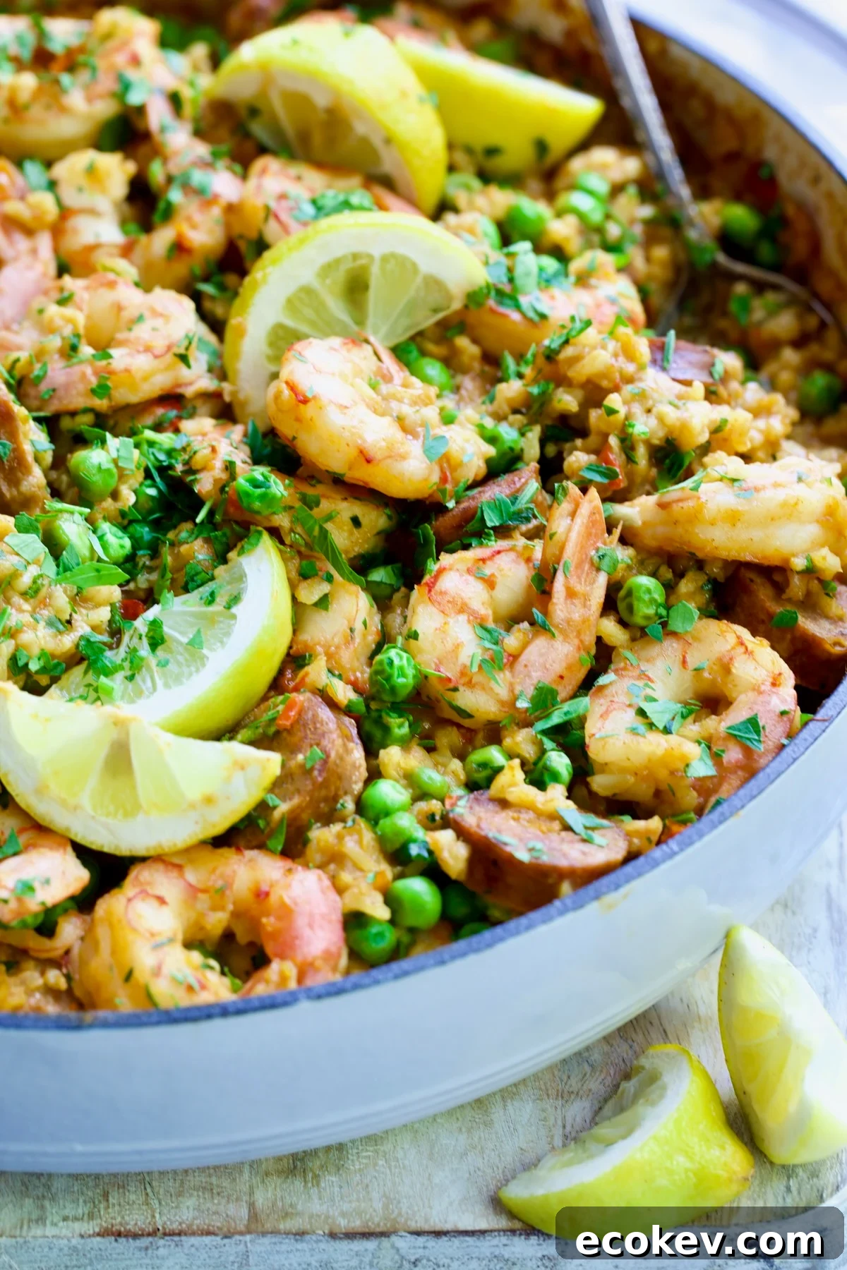 Brown Rice Paella with Shrimp and Chorizo with lemon wedges in white cast iron enamel skillet.