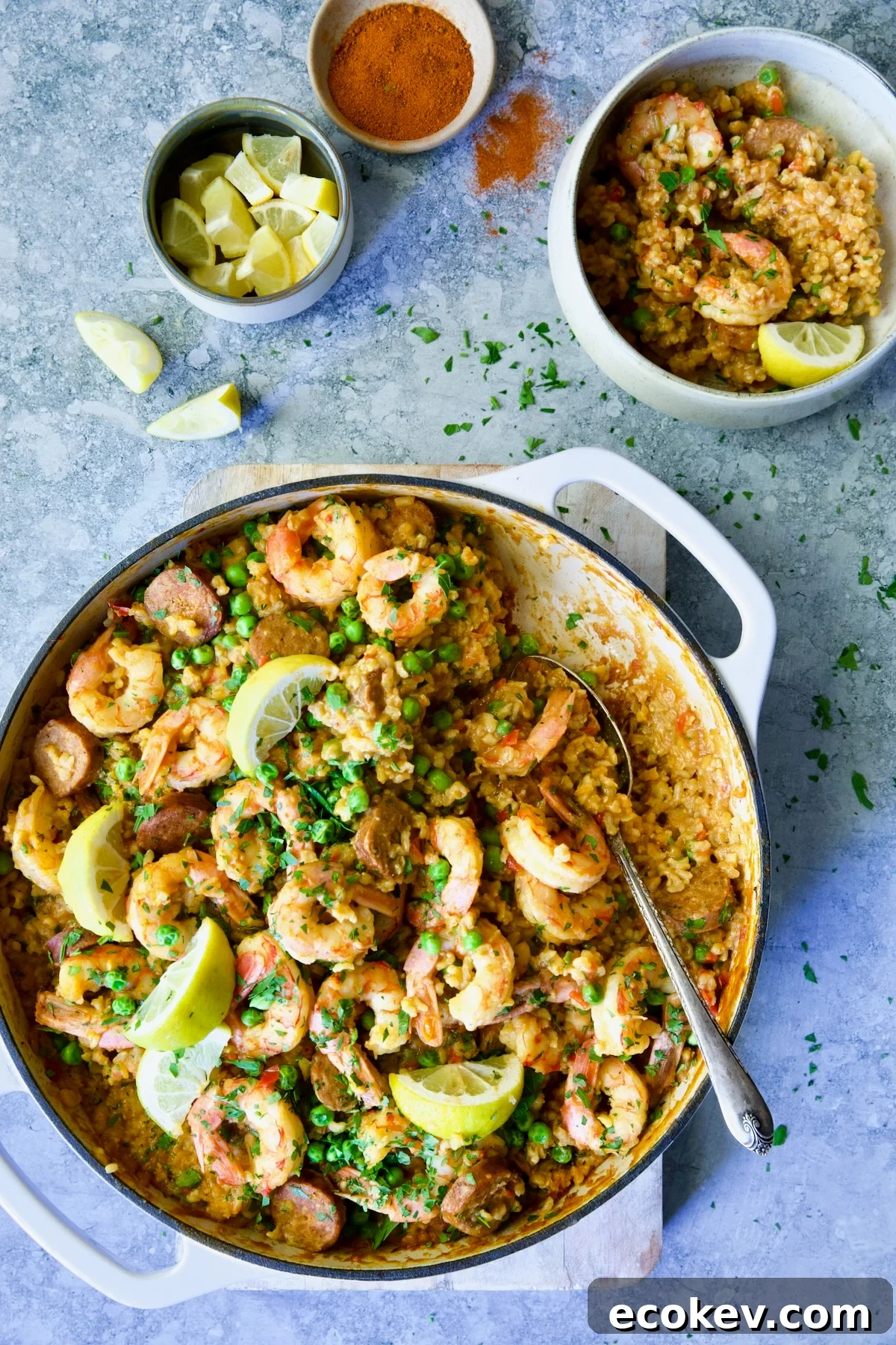 Pan of paella garnished with lemon wedges with some served into an individual bowl.