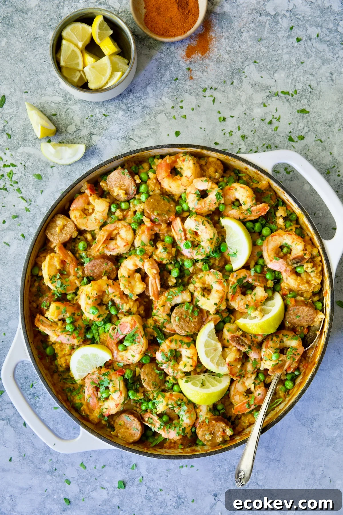 Brown Rice Paella with Shrimp and Chorizo with lemons in white enamel cast iron skillet.