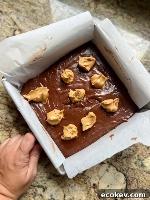 Brownie batter in pan with peanut butter dollops.