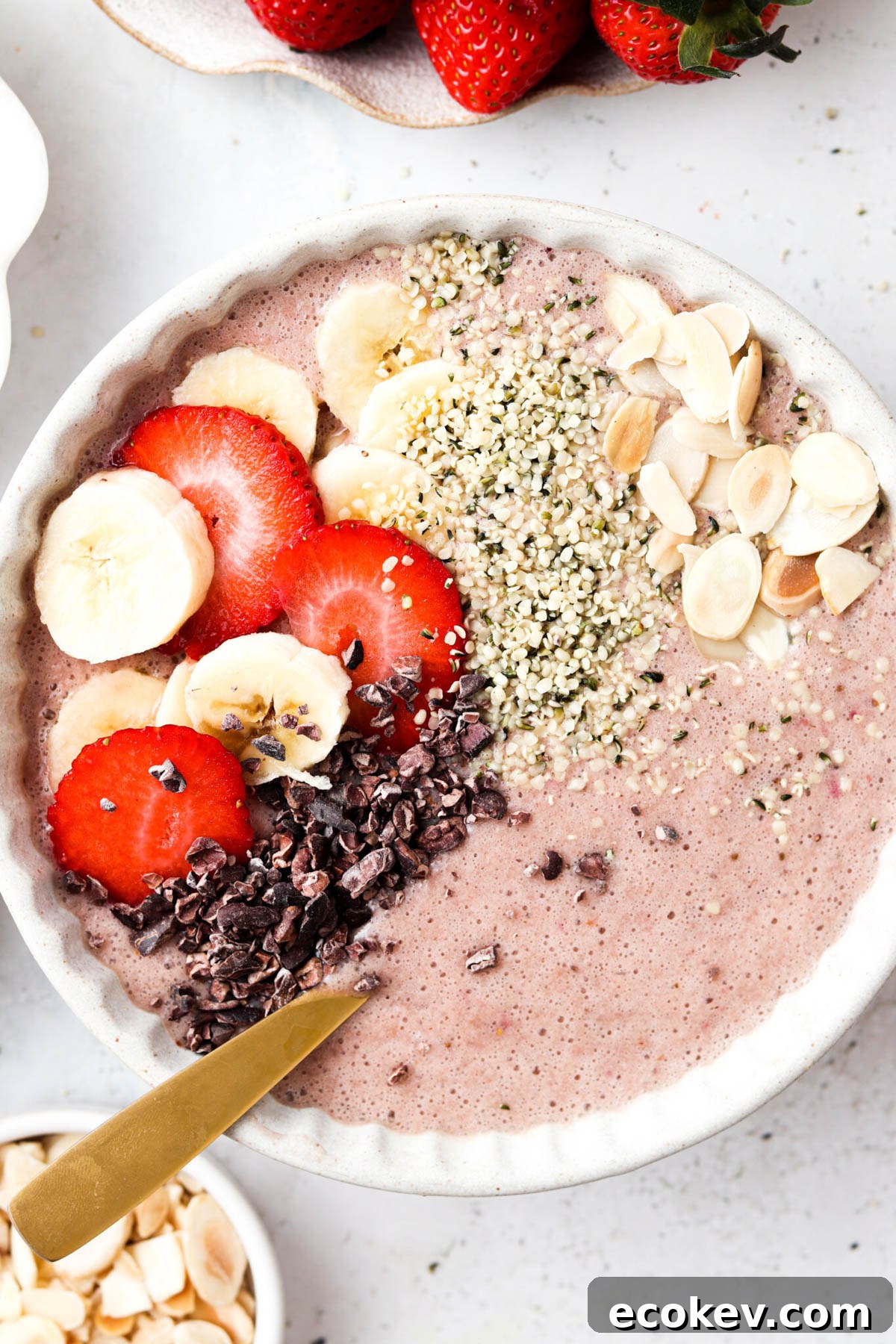 Strawberry banana smoothie bowl garnished with fresh fruit, almond slices, and seeds. 