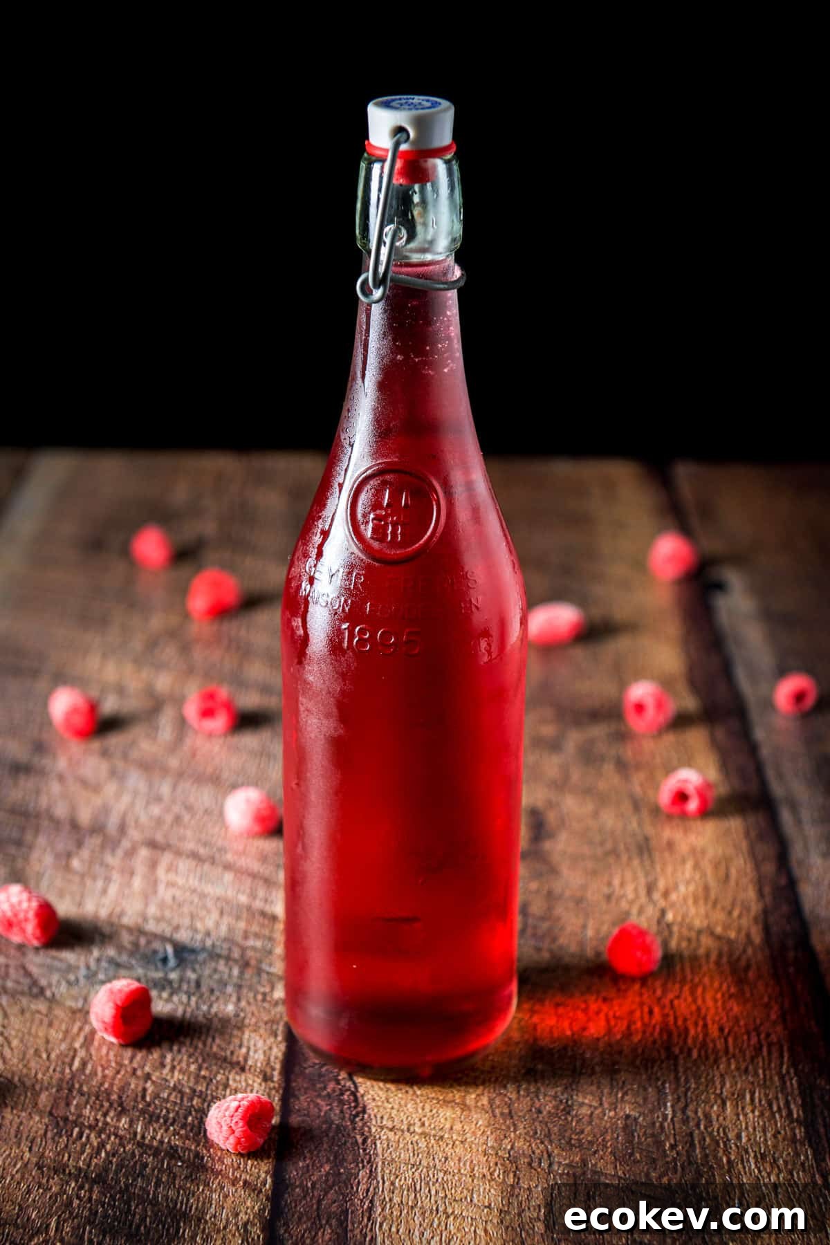 A capped bottle of red vodka with raspberries on the table