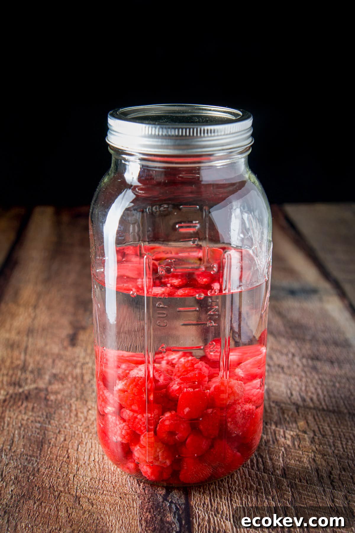 A capped jar with vodka and raspberries in it