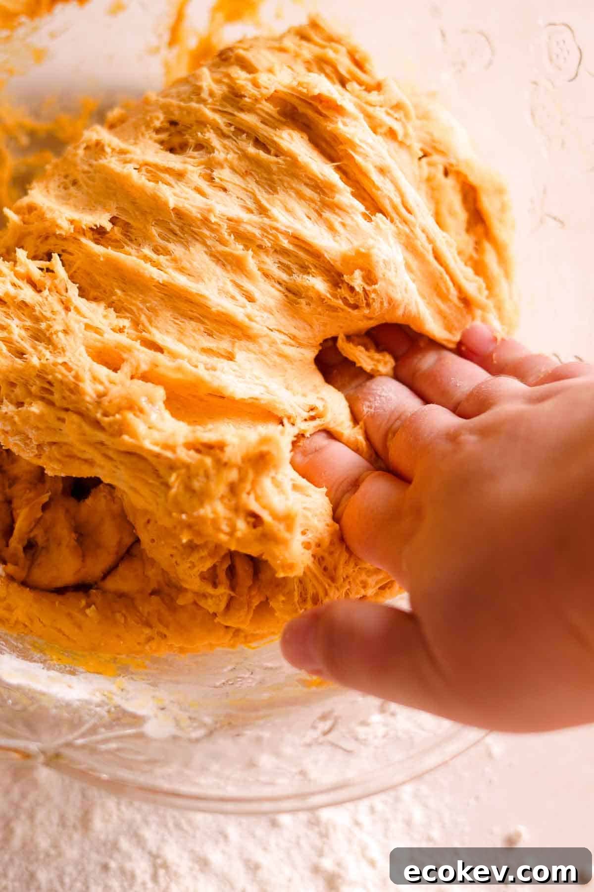 punching down the soft donut dough in a large glass bowl