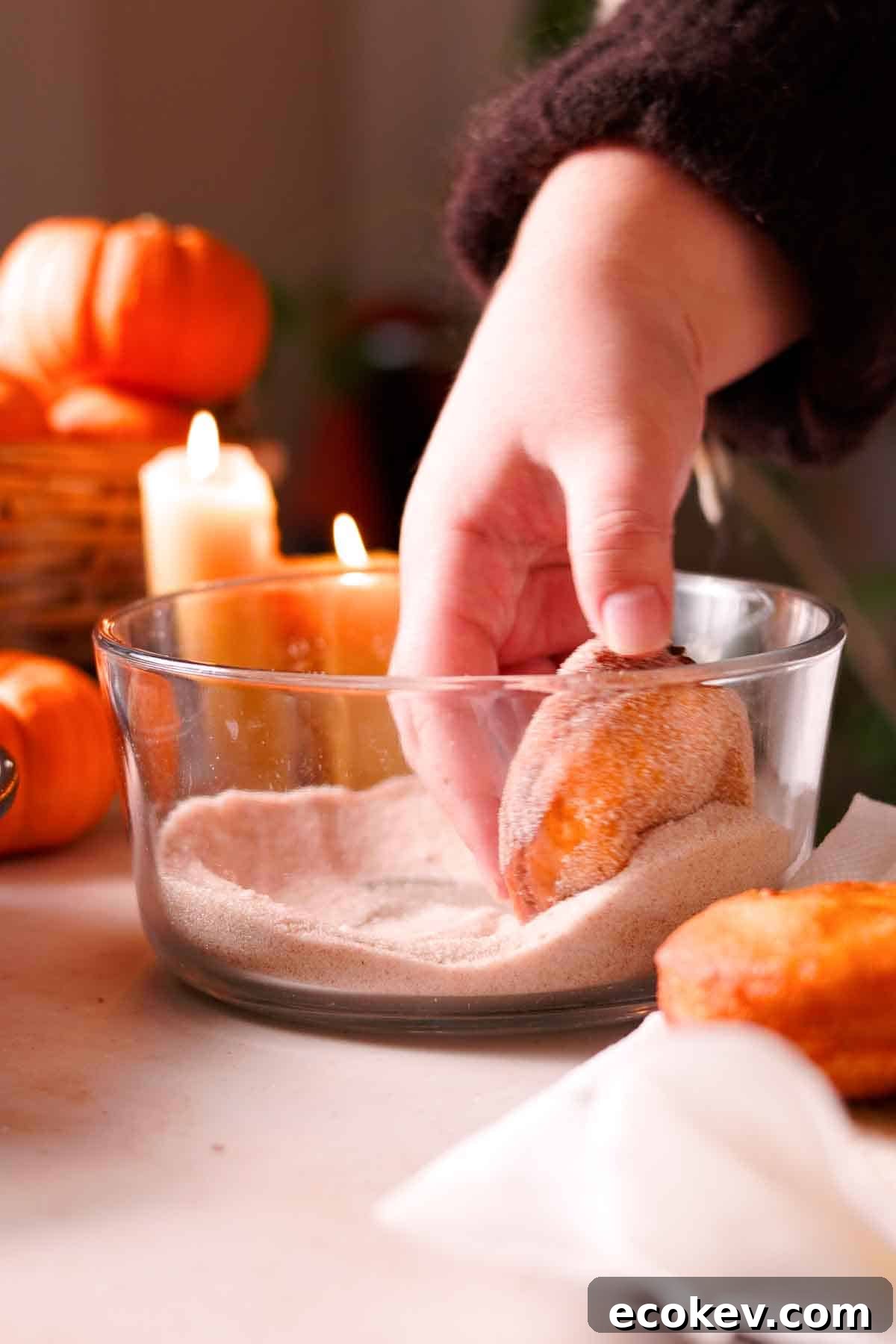 coating fried donuts with spiced sugar mixture in glass bowl
