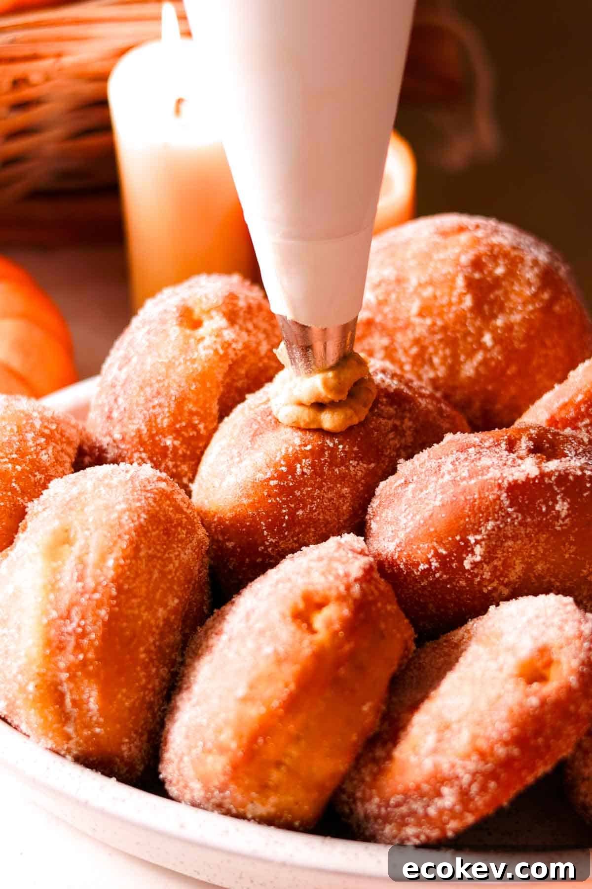 filling sugar coated donuts with cream using a white cloth pastry bag