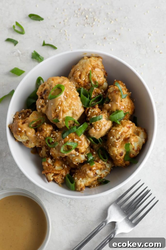 Spicy SunButter Cauliflower Wings served in a bowl and topped with sesame seeds and green onion with two forks and a bowl of SunButter sauce on the side by Flora & Vino