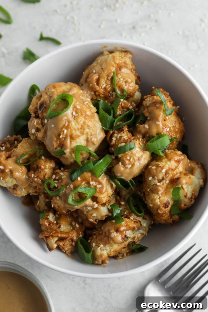 Spicy SunButter Cauliflower Wings served in a bowl and topped with sesame seeds and green onion with two forks and a bowl of SunButter sauce on the side by Flora & Vino