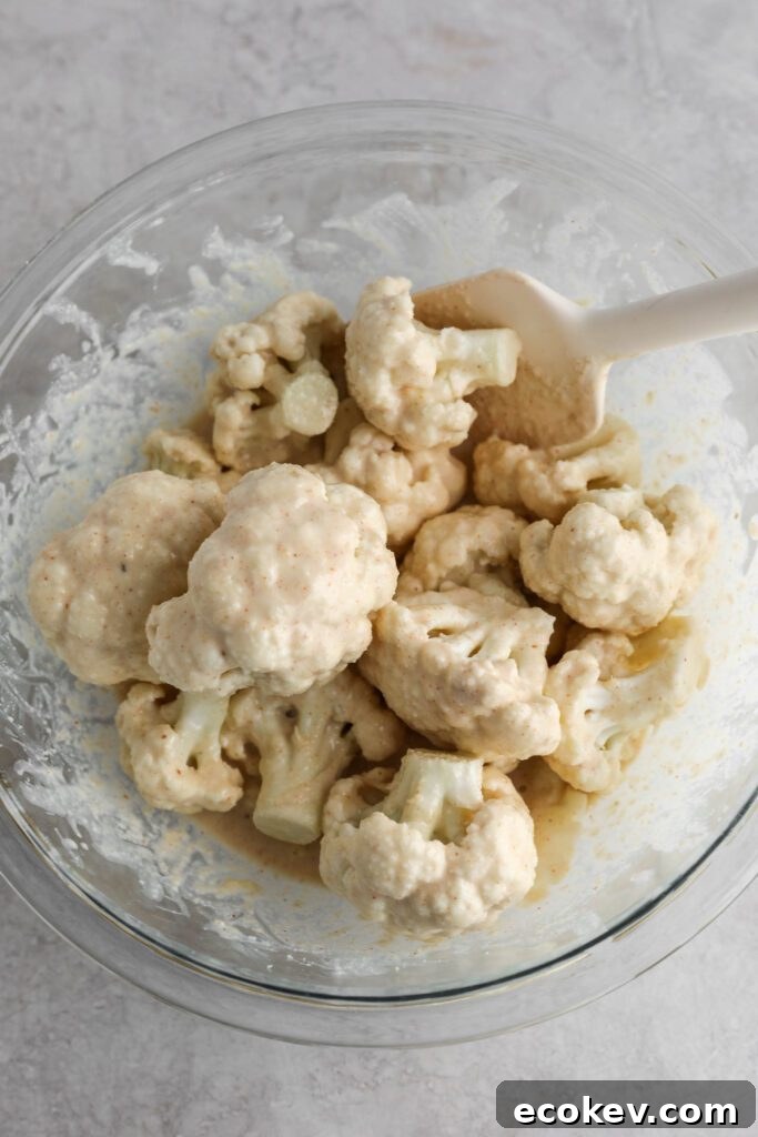 cauliflower florets mixed with batter in glass bowl with spatula by Flora & Vino
