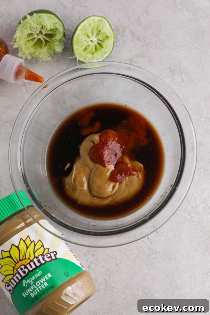 ingredients for Spicy SunButter sauce in glass bowl with sriracha, SunButter, and lime on the side by Flora & Vino