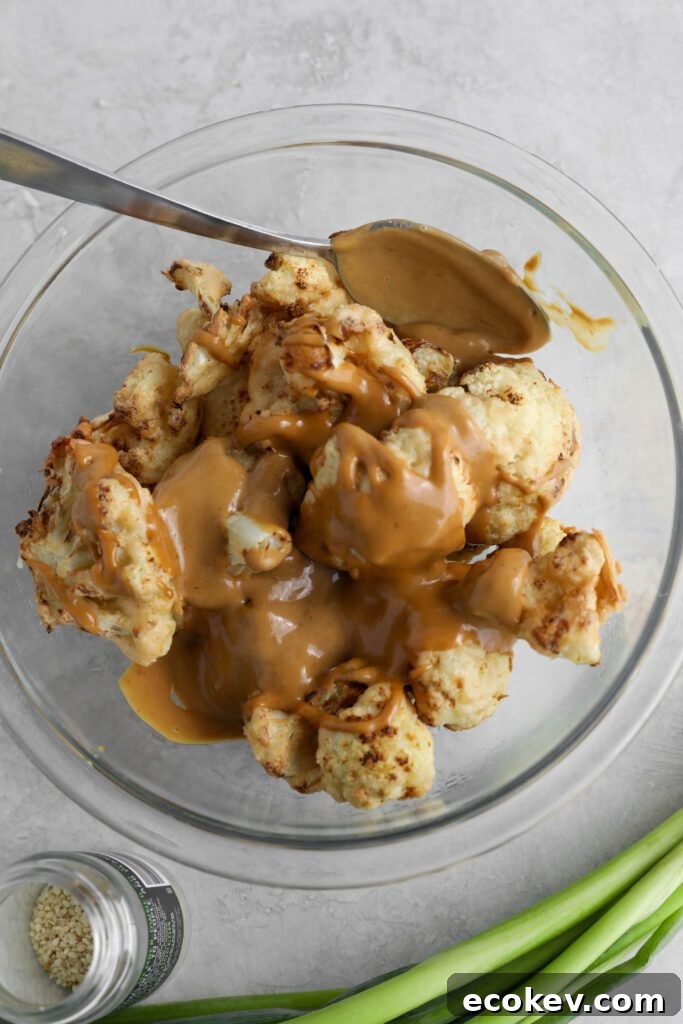 air-fried cauliflower in glass bowl topped with SunButter sauce with sesame seeds and green onion on the side by Flora & Vino