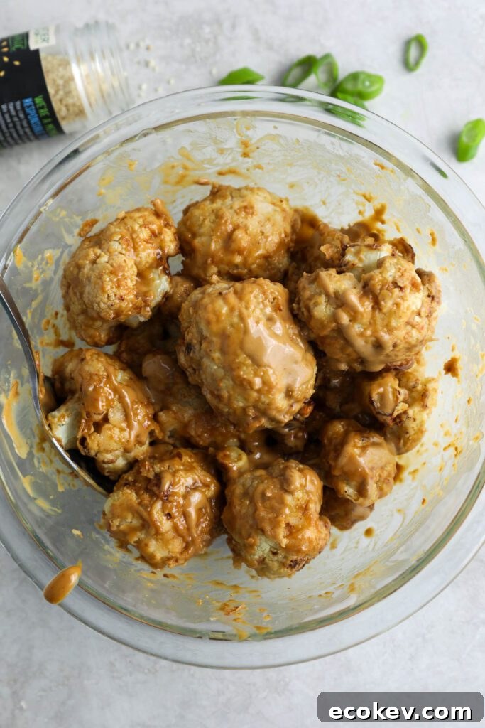 air-fried cauliflower mixed with Spicy SunButter sauce in a bowl with sesame seeds and green onion on the side by Flora & Vino