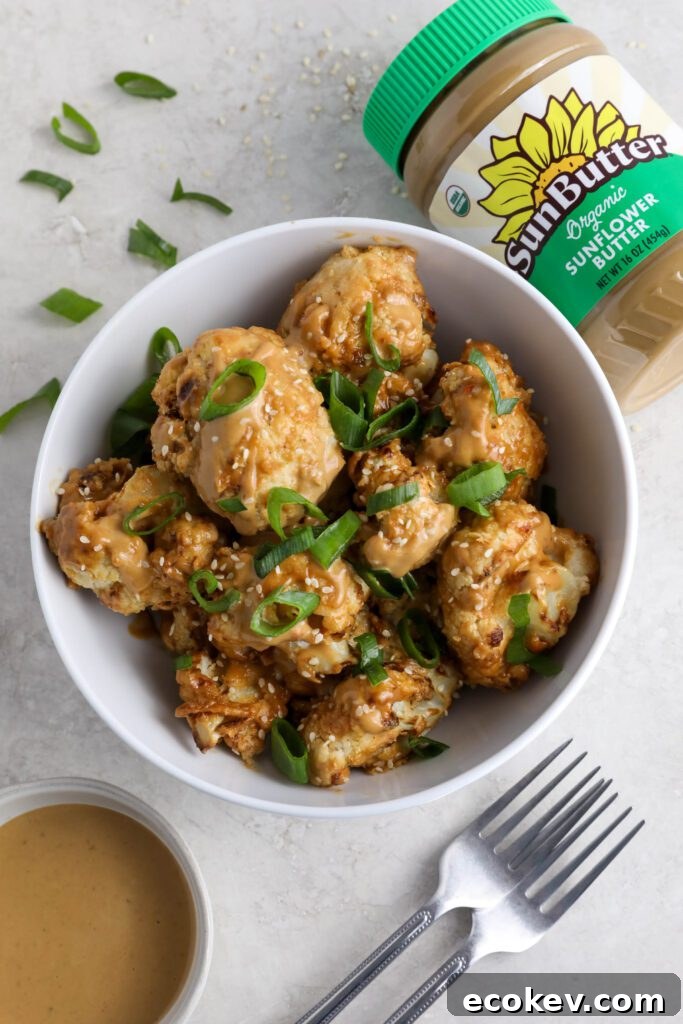 Spicy SunButter Cauliflower Wings served in a bowl and topped with sesame seeds and green onion with two forks and a bowl of SunButter sauce on the side by Flora & Vino