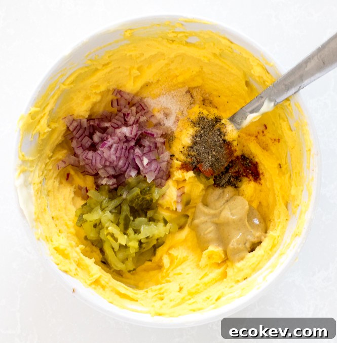 adding pickles, onions, mustard and seasoning to mashed egg yolks