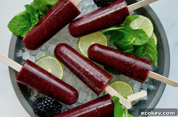 Boozy blackberry mojito popsicles over ice with limes and fresh mint