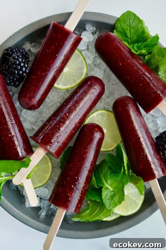 Top down view of blackberry mojito popsicles over ice with limes and fresh mint