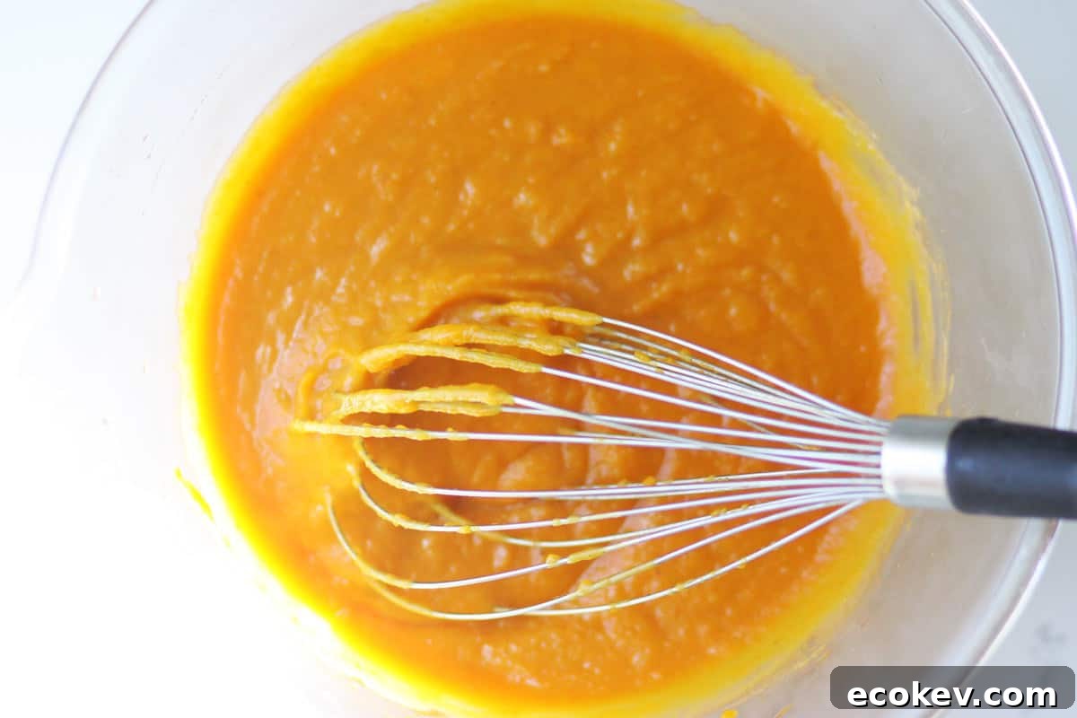 a mixture of pumpkin, coconut oil, honey and eggs in a bowl with a whisk in it