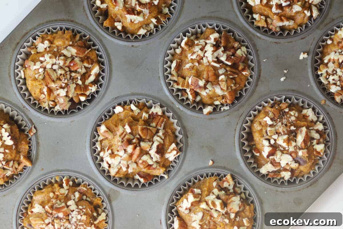 pumpkin muffins with chopped pecans in a muffin tin, ready to bake