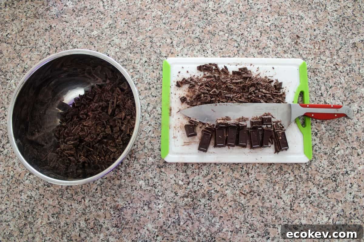 Chocolate bars being chopped on a cutting board with some already chopped in a stainless steel bowl.