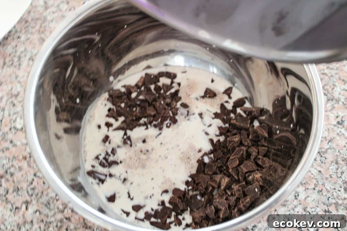 A stainless bowl with chocolate that hot heavy cream was just added to from a stainless pot, the last drips being poured in.