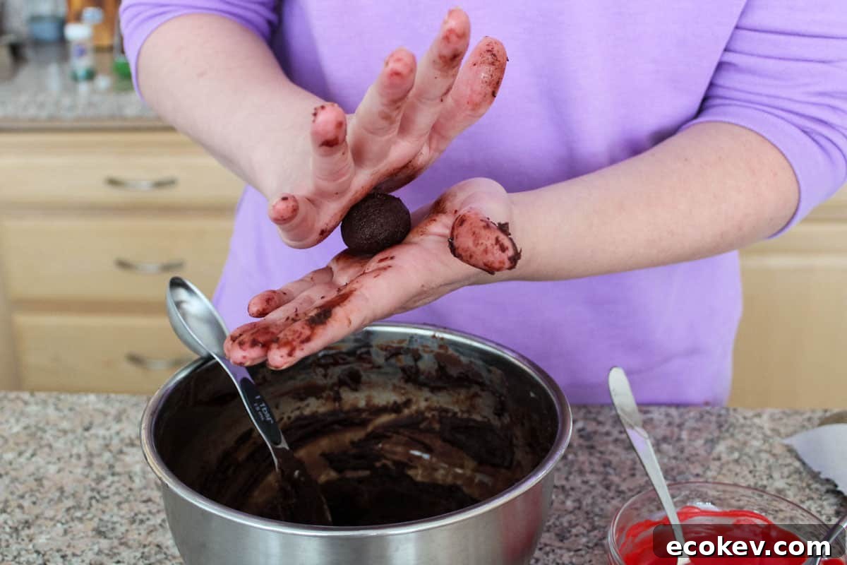 A tablespoon measuring spoon in a bowl of ganache, with someone rolling a ball of one between their hands.